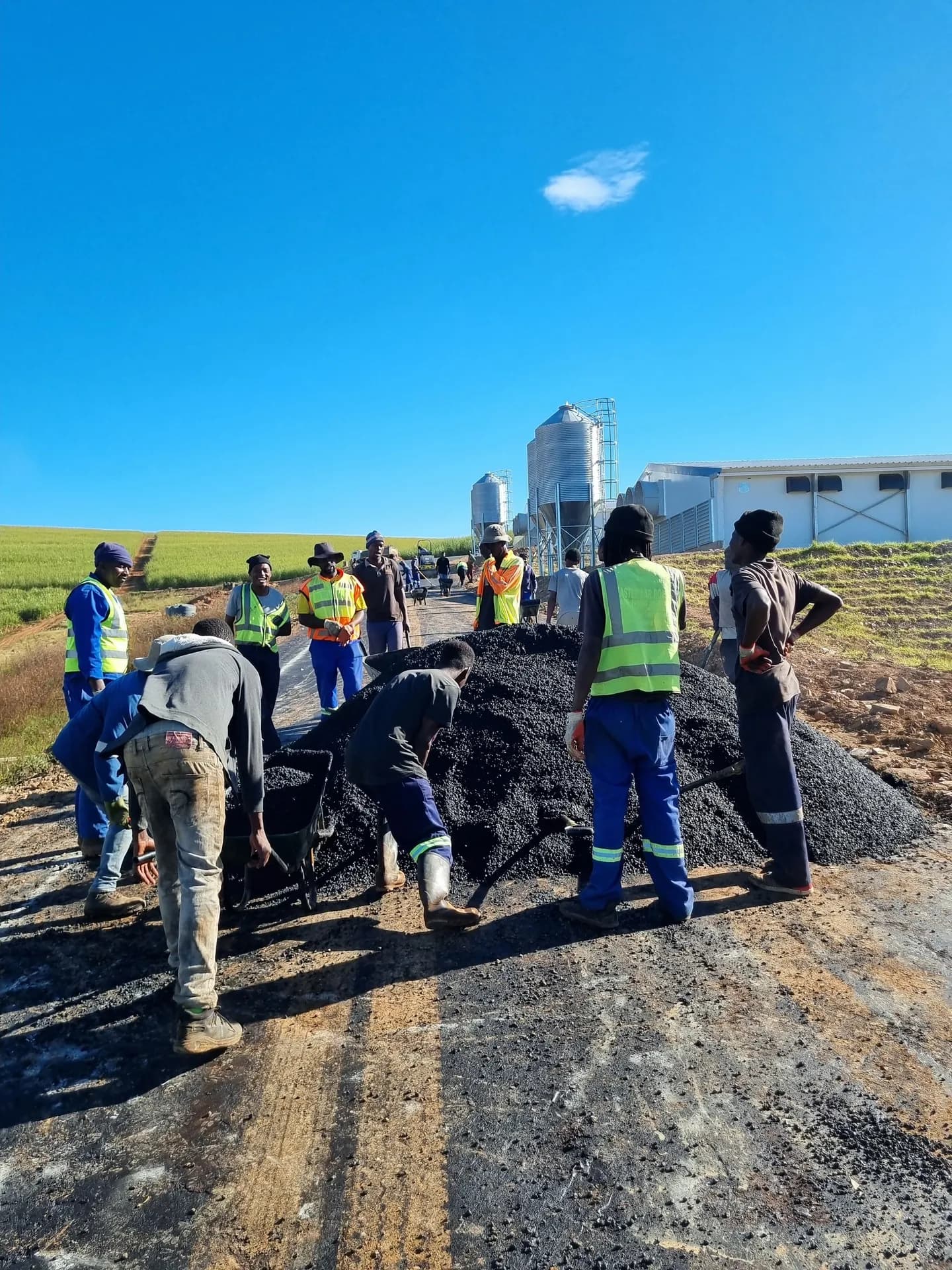 Team loading asphalt by hand near farm silos